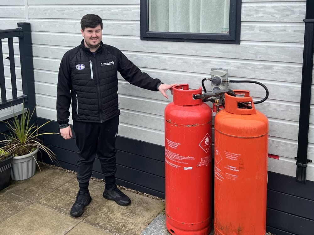 A BHE engineer stood next to red LPG canisters he has just installed at a caravan in a holiday home near Lancashire