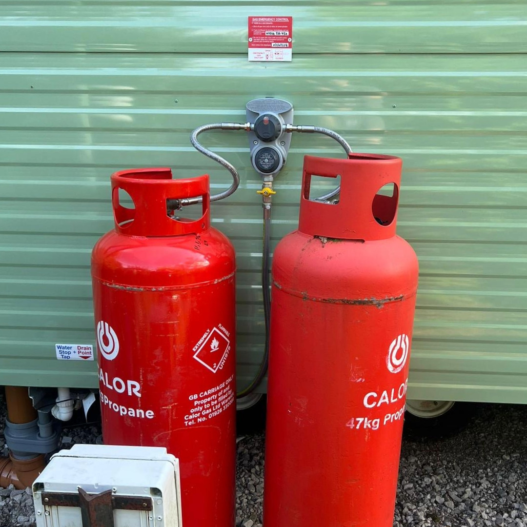 2 red LPG canisters attached to a green caravan holiday home